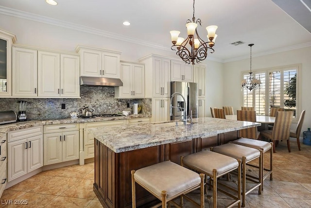 kitchen featuring appliances with stainless steel finishes, under cabinet range hood, a kitchen breakfast bar, tasteful backsplash, and a chandelier