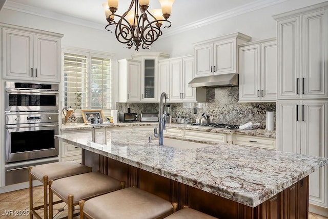 kitchen featuring under cabinet range hood, ornamental molding, decorative backsplash, appliances with stainless steel finishes, and a sink