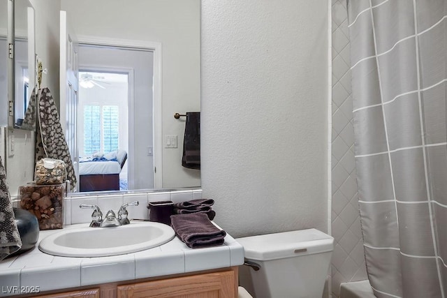 bathroom featuring vanity, toilet, a textured wall, and connected bathroom