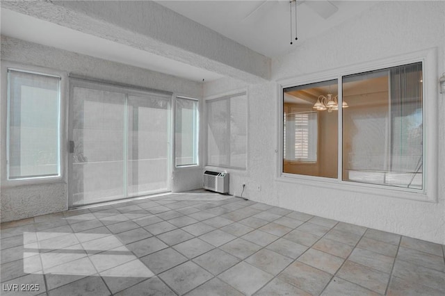 interior space with ceiling fan with notable chandelier, a textured wall, and a wall mounted AC