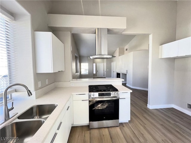 kitchen with light countertops, stainless steel gas range, a sink, white cabinets, and wall chimney range hood