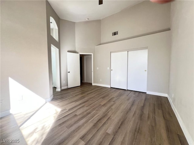 unfurnished bedroom featuring baseboards, visible vents, a high ceiling, and wood finished floors