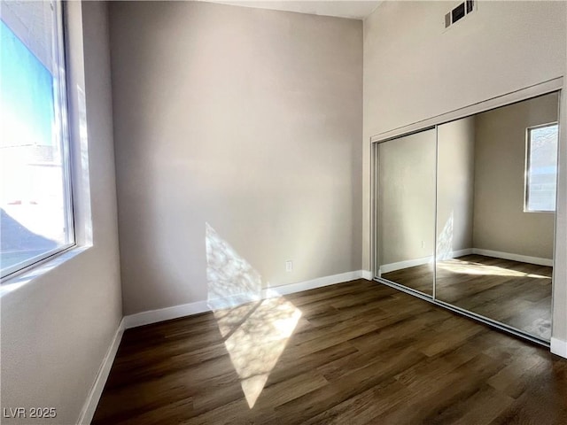 unfurnished bedroom with visible vents, multiple windows, dark wood-type flooring, and baseboards