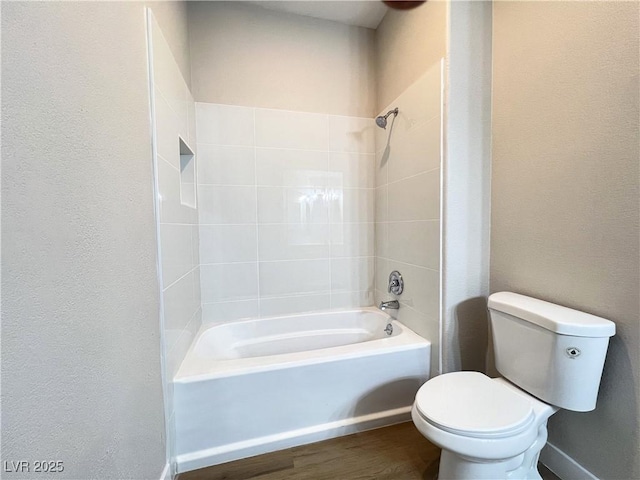 bathroom with toilet, shower / washtub combination, wood finished floors, and a textured wall