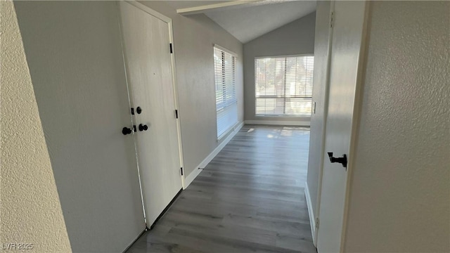 hall with lofted ceiling, wood finished floors, baseboards, and a textured wall