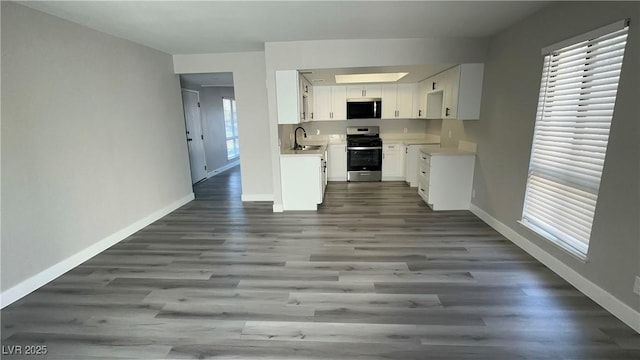 kitchen with a sink, baseboards, appliances with stainless steel finishes, and dark wood-style flooring