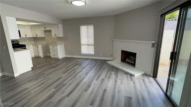 kitchen featuring open floor plan, wood finished floors, stainless steel electric range, white cabinets, and a fireplace