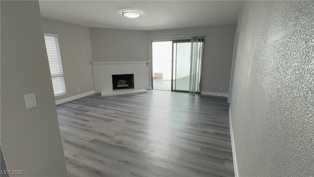 unfurnished living room with a textured wall, a brick fireplace, baseboards, and wood finished floors