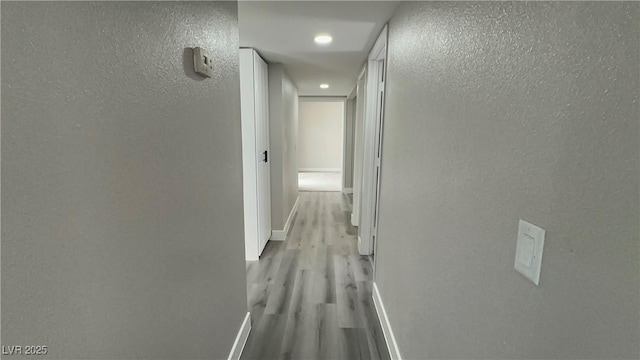 hallway featuring a textured wall, baseboards, and wood finished floors