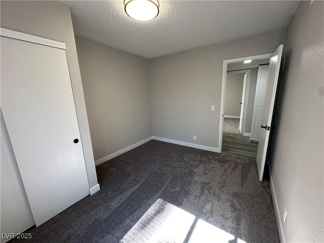 unfurnished bedroom featuring baseboards, a textured ceiling, and dark carpet