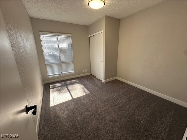 unfurnished bedroom with baseboards, a closet, a textured ceiling, a textured wall, and dark colored carpet