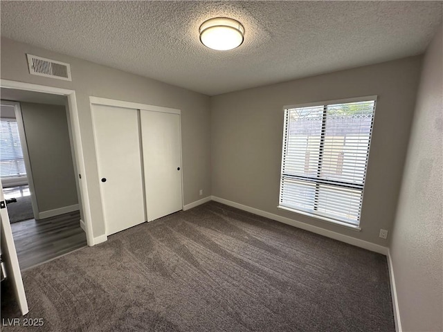 unfurnished bedroom featuring dark carpet, baseboards, visible vents, and a closet