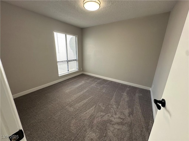 empty room featuring dark carpet, a textured ceiling, and baseboards