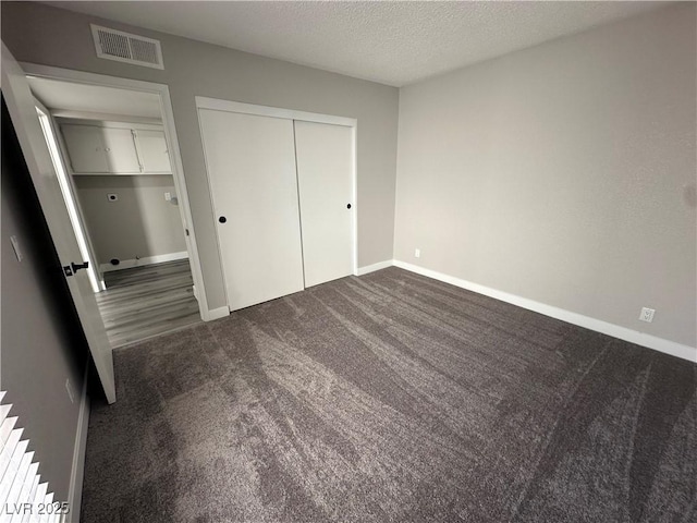 unfurnished bedroom with visible vents, dark carpet, a textured ceiling, and baseboards