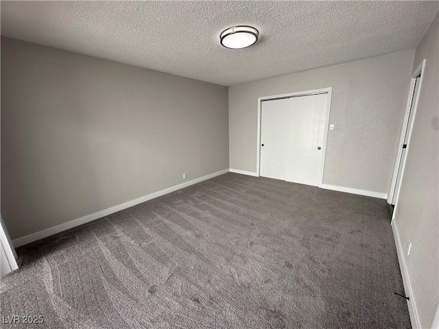 empty room featuring baseboards, dark colored carpet, and a textured ceiling