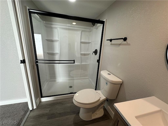 full bathroom featuring toilet, wood finished floors, a shower stall, and a textured wall