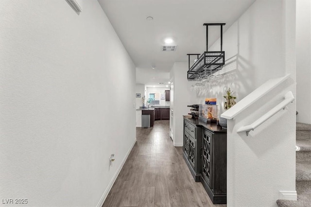 hallway with stairway, wood finished floors, visible vents, and baseboards