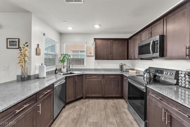 kitchen featuring light stone counters, visible vents, light wood-style flooring, dark brown cabinetry, and appliances with stainless steel finishes