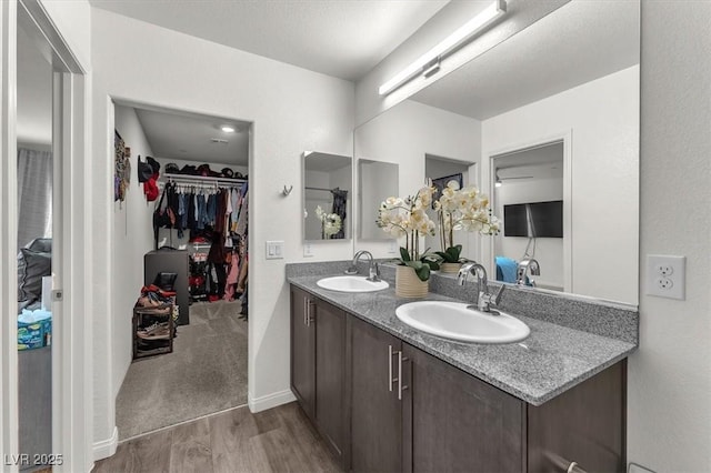 full bathroom with a sink, double vanity, wood finished floors, and a spacious closet