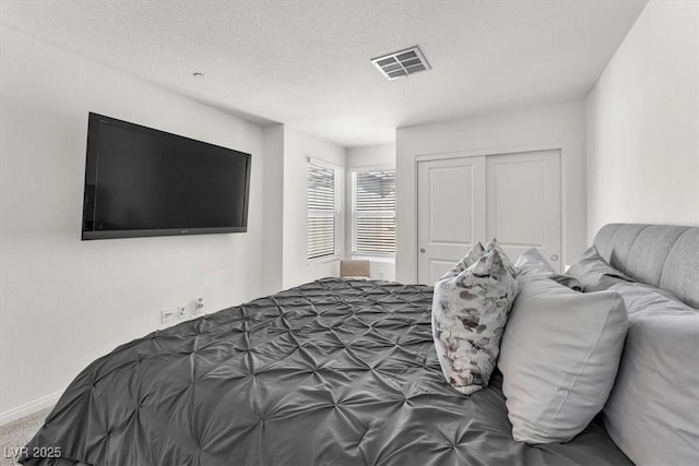 carpeted bedroom featuring visible vents, baseboards, a textured ceiling, and a closet