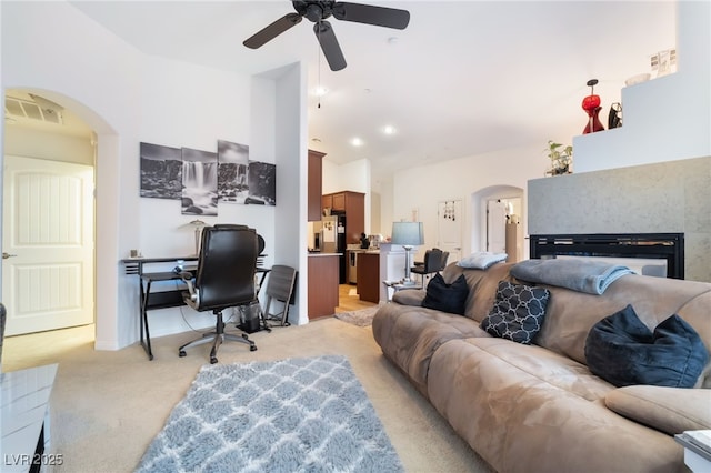 living room with light colored carpet, vaulted ceiling, arched walkways, a glass covered fireplace, and a ceiling fan