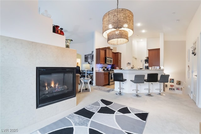 kitchen with a breakfast bar, stainless steel appliances, light carpet, brown cabinets, and a chandelier