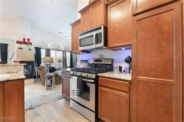 kitchen featuring light wood-type flooring, brown cabinets, open floor plan, appliances with stainless steel finishes, and vaulted ceiling