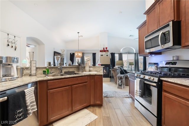 kitchen with a sink, stainless steel appliances, light stone counters, and brown cabinetry