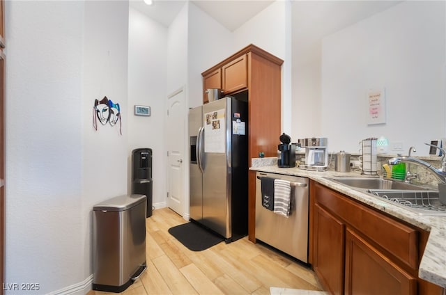 kitchen with light stone counters, light wood finished floors, a sink, stainless steel appliances, and brown cabinets