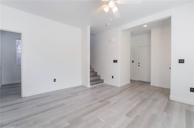 spare room with stairway, baseboards, ceiling fan, and light wood finished floors