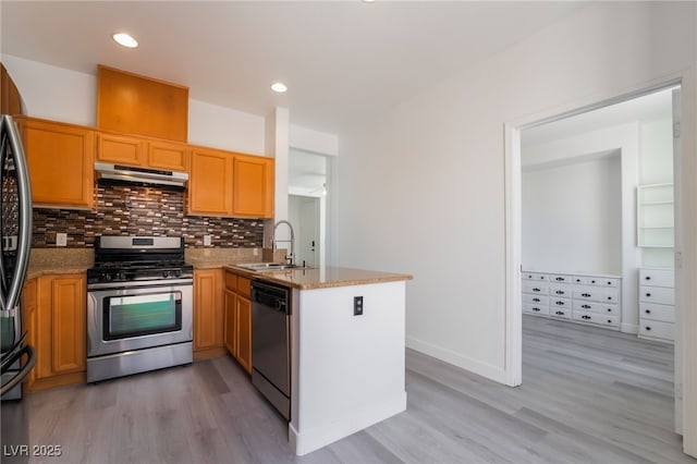 kitchen with backsplash, under cabinet range hood, appliances with stainless steel finishes, a peninsula, and a sink