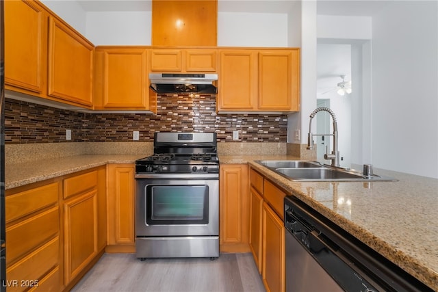 kitchen with under cabinet range hood, decorative backsplash, light wood-style flooring, appliances with stainless steel finishes, and a sink