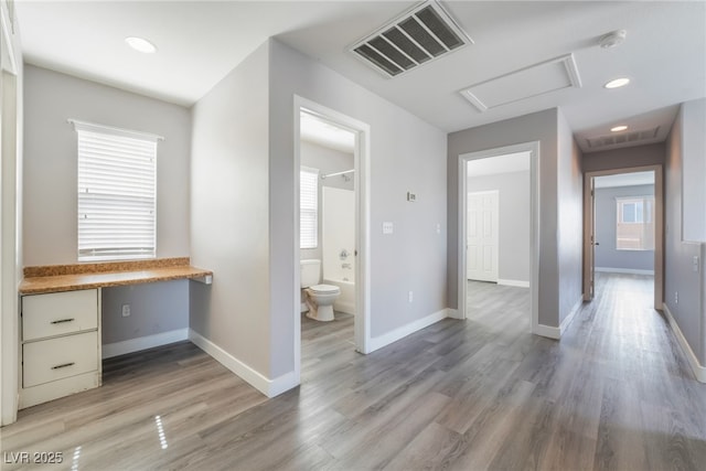 hall with light wood-style floors, attic access, a healthy amount of sunlight, and visible vents