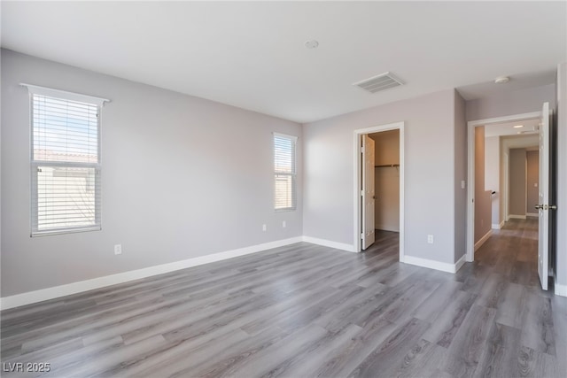 unfurnished bedroom with visible vents, baseboards, wood finished floors, and a spacious closet