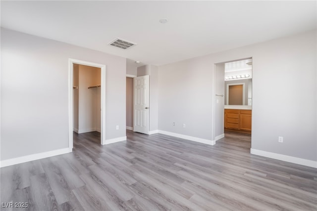 unfurnished bedroom featuring a walk in closet, baseboards, visible vents, and light wood-type flooring