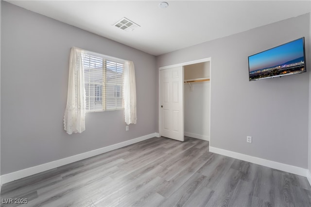 unfurnished bedroom with wood finished floors, baseboards, visible vents, and a closet