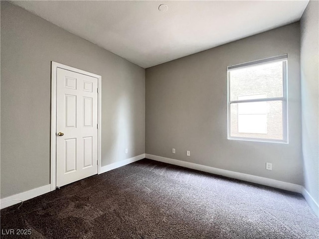 spare room featuring baseboards and dark colored carpet