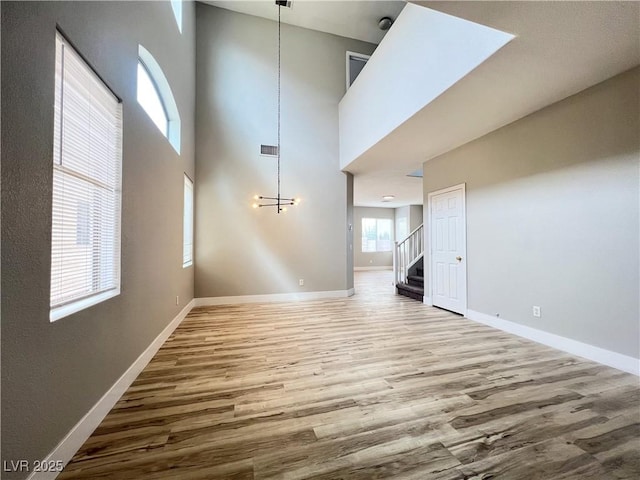 unfurnished living room with wood finished floors, baseboards, stairs, a towering ceiling, and a chandelier