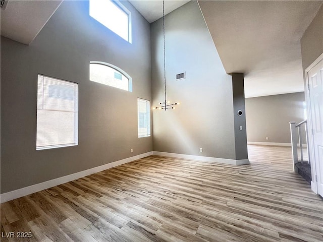 unfurnished living room featuring visible vents, a towering ceiling, baseboards, and wood finished floors