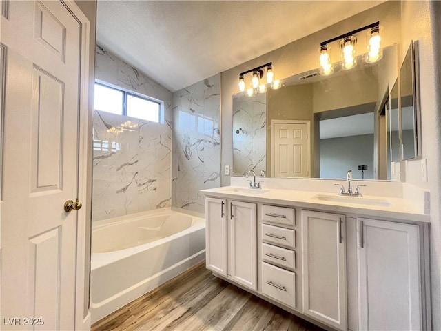 bathroom featuring double vanity, a bath, wood finished floors, and a sink