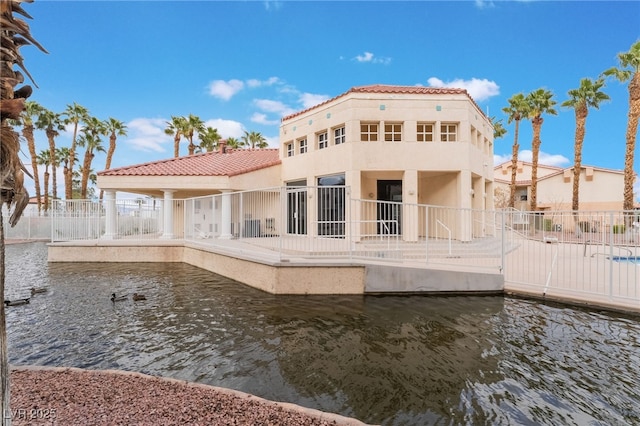 back of property with a tiled roof, fence, a water view, and stucco siding