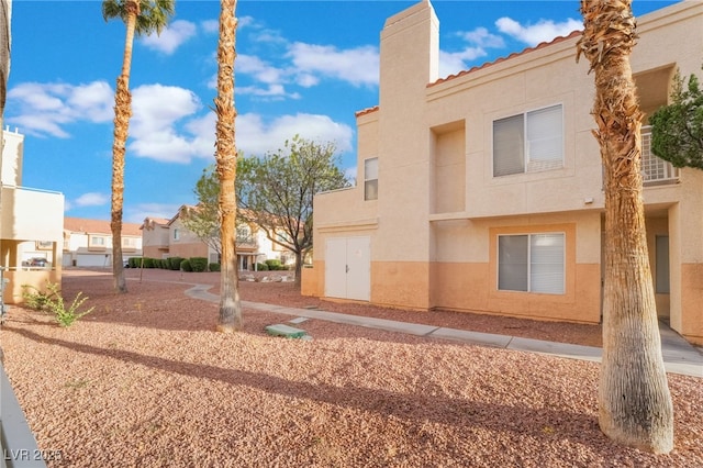 rear view of house featuring a residential view, stucco siding, a tiled roof, and a chimney