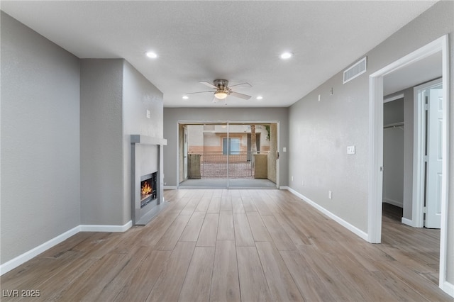 unfurnished living room with visible vents, baseboards, a lit fireplace, and wood finished floors