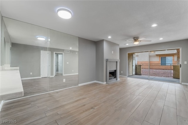 unfurnished living room featuring visible vents, baseboards, a fireplace, ceiling fan, and light wood-type flooring