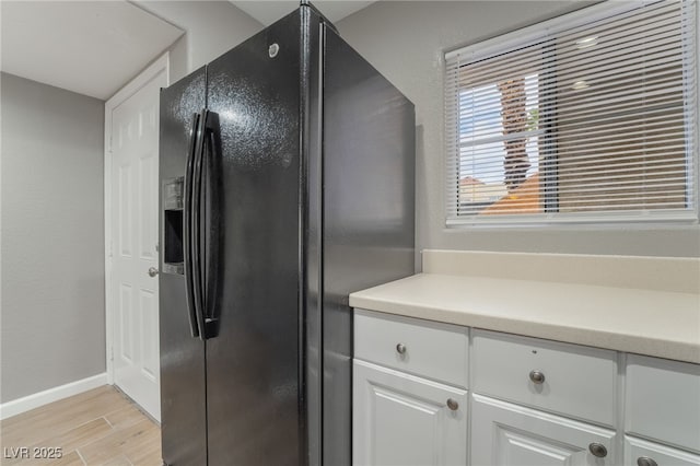 kitchen with baseboards, wood tiled floor, light countertops, white cabinets, and black refrigerator with ice dispenser