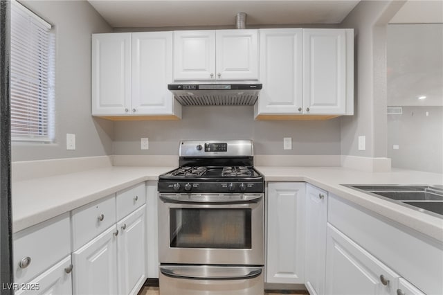 kitchen featuring under cabinet range hood, stainless steel gas stove, white cabinets, and light countertops