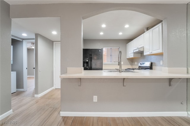 kitchen featuring range with gas stovetop, light wood finished floors, a peninsula, arched walkways, and black fridge