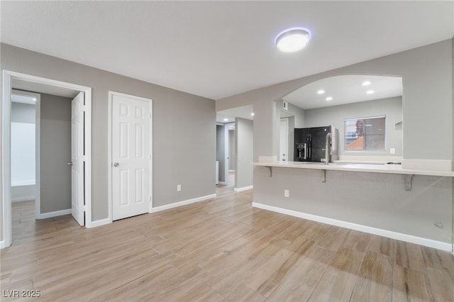 unfurnished living room featuring recessed lighting, arched walkways, baseboards, and light wood finished floors