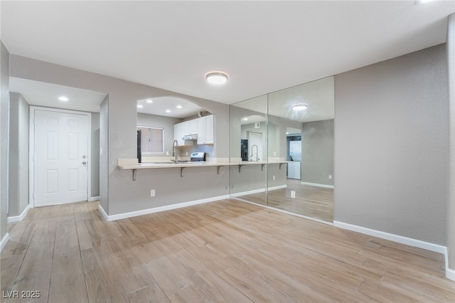 unfurnished living room with light wood-style flooring, baseboards, and a sink