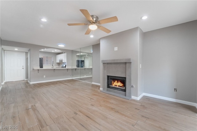 unfurnished living room with a sink, baseboards, a lit fireplace, and light wood finished floors